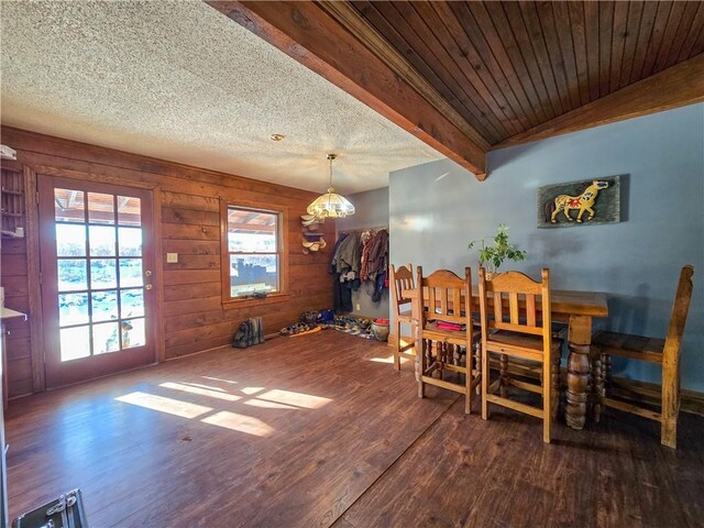 dining room featuring wood walls, wood ceiling, a textured ceiling, dark hardwood / wood-style floors, and beamed ceiling