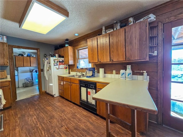 kitchen featuring dishwashing machine, sink, washing machine and dryer, dark hardwood / wood-style floors, and a textured ceiling