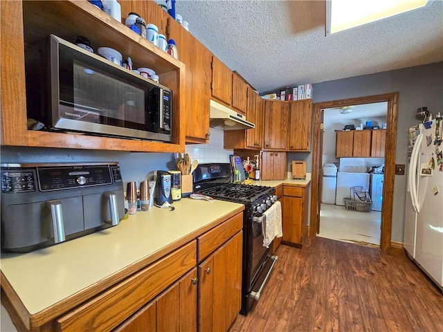 kitchen with dark wood-type flooring, a textured ceiling, white fridge, washer / clothes dryer, and gas range oven