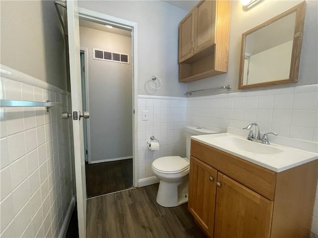 bathroom featuring toilet, wood finished floors, vanity, visible vents, and tile walls