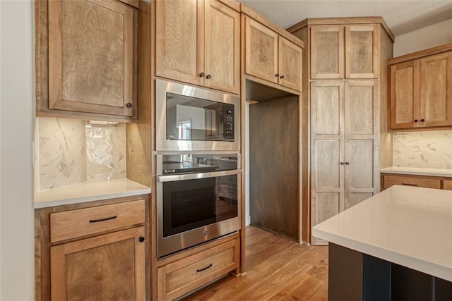 kitchen featuring light wood-style floors, tasteful backsplash, light countertops, oven, and built in microwave