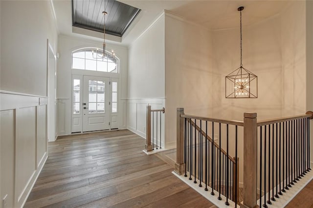 entryway with crown molding, a decorative wall, wood finished floors, a raised ceiling, and a notable chandelier