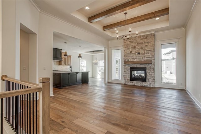 unfurnished living room featuring dark wood-style flooring, ornamental molding, a sink, a chandelier, and beamed ceiling