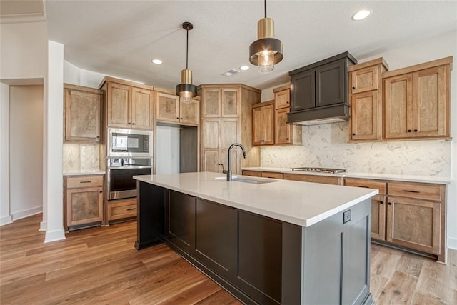 kitchen featuring decorative light fixtures, light wood-style floors, decorative backsplash, stainless steel appliances, and a sink