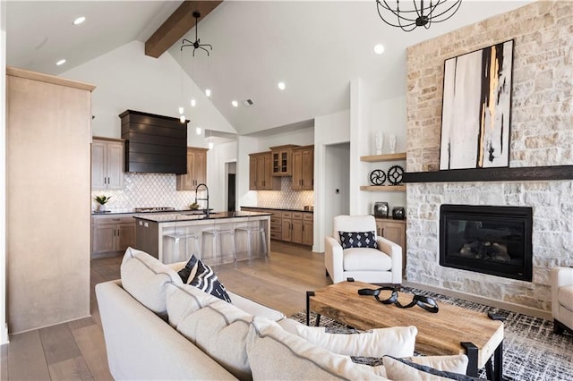 living area with beam ceiling, a stone fireplace, light wood finished floors, and recessed lighting