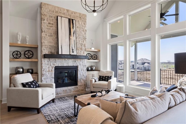 living room featuring built in shelves, a notable chandelier, a stone fireplace, and wood finished floors