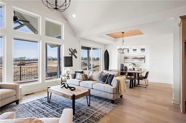 living room with a tray ceiling, baseboards, light wood-type flooring, and a notable chandelier