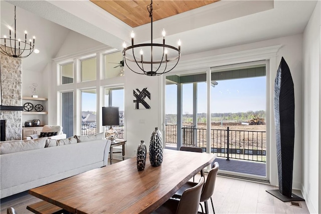 dining area with light wood-type flooring, a stone fireplace, a chandelier, lofted ceiling, and built in shelves