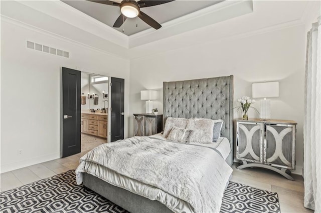 bedroom featuring light wood-type flooring, ornamental molding, visible vents, a raised ceiling, and baseboards