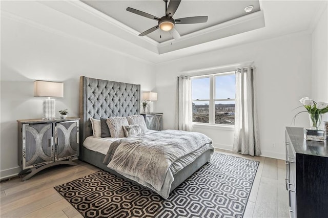 bedroom featuring a tray ceiling, crown molding, a ceiling fan, and light wood-style flooring