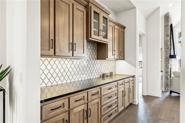 kitchen featuring dark wood finished floors, glass insert cabinets, dark countertops, decorative backsplash, and baseboards