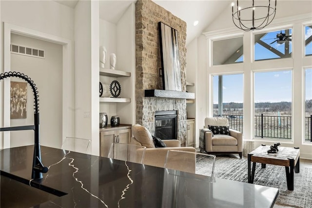 interior space featuring a stone fireplace, dark countertops, visible vents, built in shelves, and ceiling fan with notable chandelier