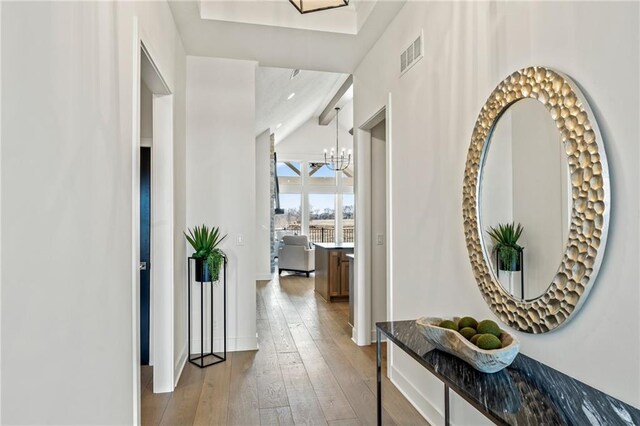 corridor with baseboards, a chandelier, wood-type flooring, and visible vents