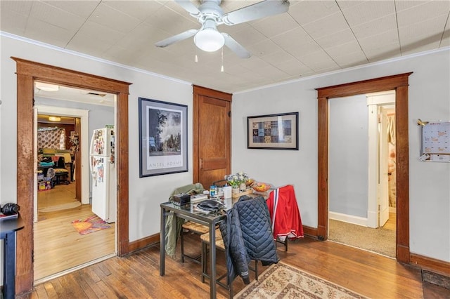 dining room featuring ceiling fan, baseboards, crown molding, and wood finished floors