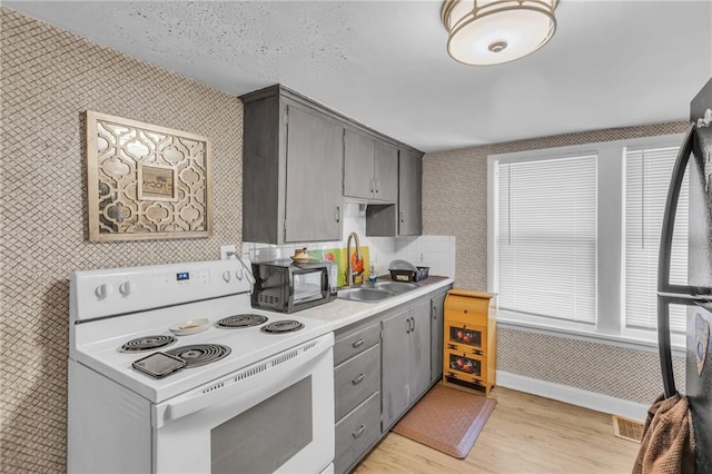 kitchen featuring gray cabinetry, a sink, light countertops, black appliances, and wallpapered walls