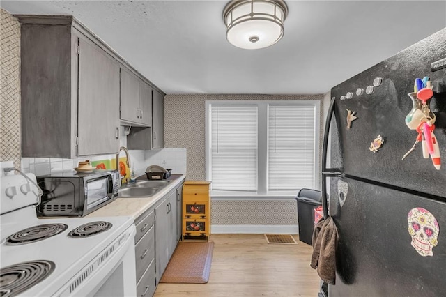 kitchen featuring white electric stove, wallpapered walls, freestanding refrigerator, and light wood-style floors