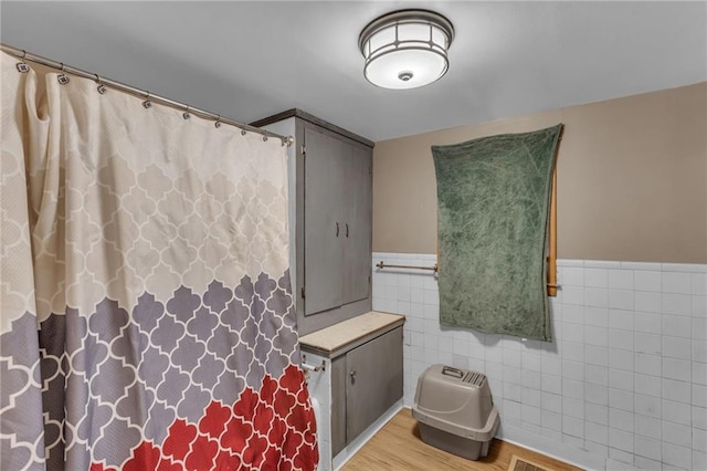 bathroom featuring a wainscoted wall, wood finished floors, and tile walls