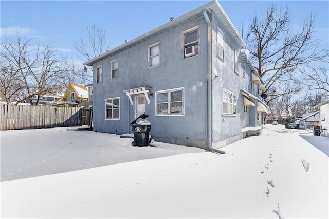 snow covered back of property with fence and stucco siding