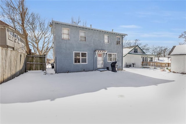 snow covered house featuring fence and stucco siding