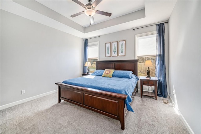 bedroom with a tray ceiling, multiple windows, baseboards, and light carpet