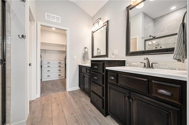 full bath with vanity, visible vents, wood finish floors, tiled shower, and lofted ceiling