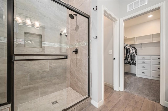 full bathroom with visible vents, a walk in closet, a stall shower, baseboards, and wood tiled floor