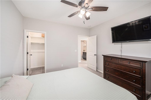 bedroom with light carpet, a spacious closet, a ceiling fan, and baseboards