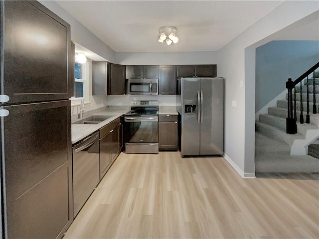 kitchen featuring baseboards, appliances with stainless steel finishes, light countertops, light wood-type flooring, and a sink