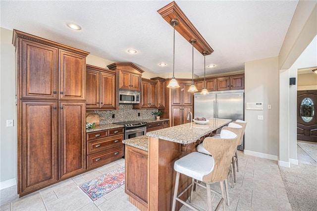 kitchen with pendant lighting, a kitchen island with sink, backsplash, stainless steel appliances, and light stone countertops