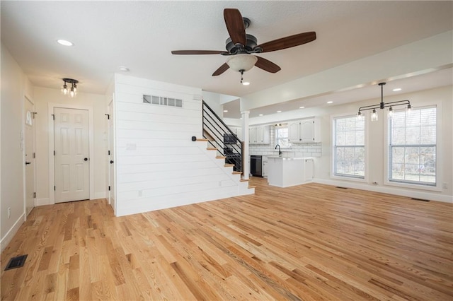 unfurnished living room with stairs, light wood-style floors, visible vents, and a ceiling fan