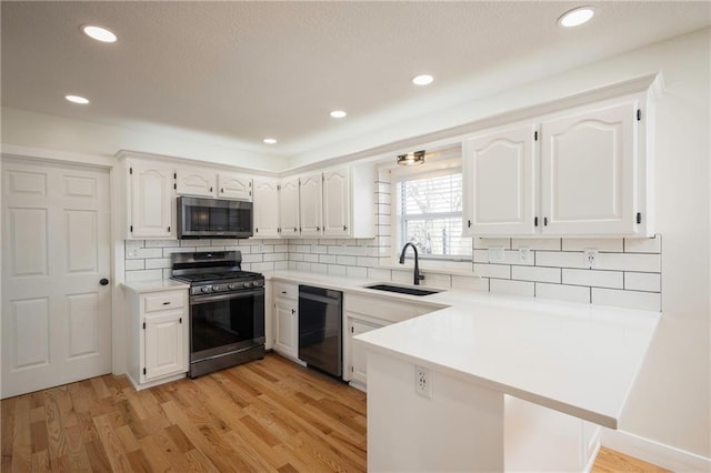 kitchen featuring light wood-style flooring, a sink, white cabinetry, appliances with stainless steel finishes, and a peninsula