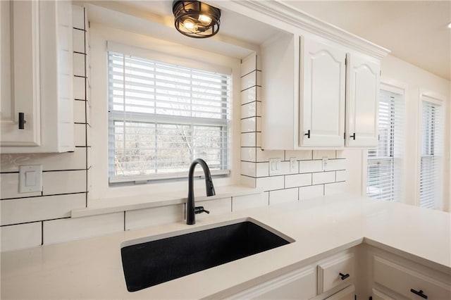 kitchen with tasteful backsplash, white cabinetry, light countertops, and a sink