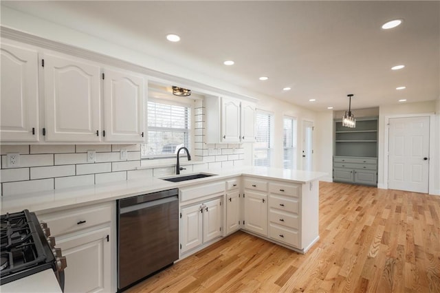 kitchen with range, a peninsula, stainless steel dishwasher, white cabinetry, and a sink