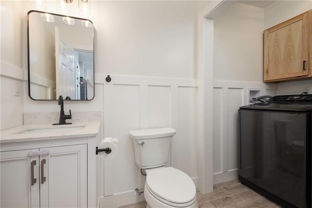 bathroom featuring toilet, a decorative wall, washer / clothes dryer, and wainscoting