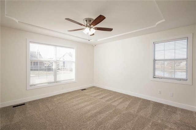 empty room with baseboards, visible vents, carpet floors, ceiling fan, and a raised ceiling