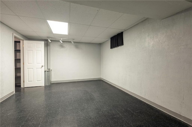 finished basement with a paneled ceiling, dark floors, and baseboards