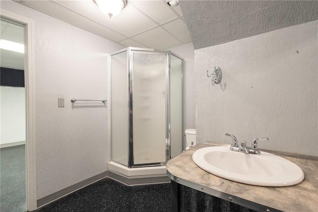 full bath featuring vanity, a shower stall, a textured wall, and a drop ceiling