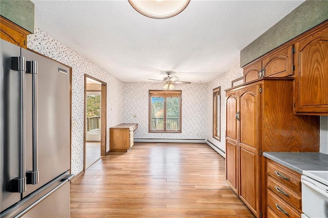 kitchen with high end refrigerator, a baseboard heating unit, a textured ceiling, and light wood-type flooring