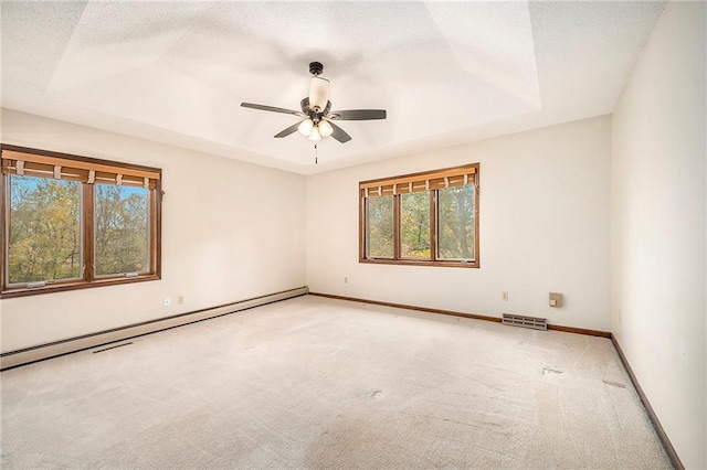 empty room featuring a textured ceiling, baseboard heating, a tray ceiling, ceiling fan, and carpet