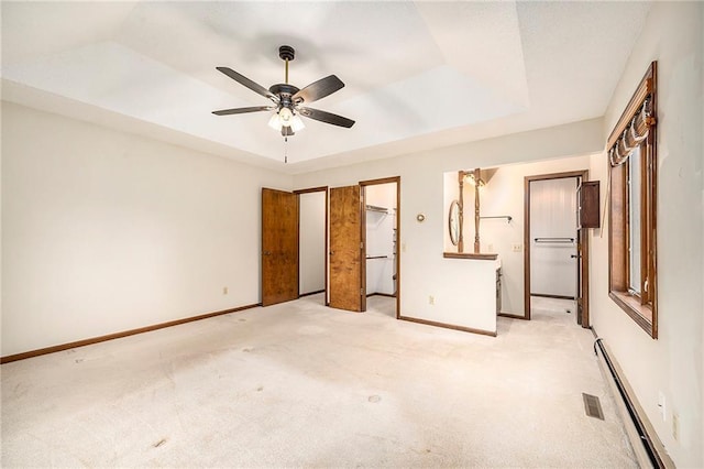 unfurnished bedroom with a baseboard radiator, fridge, a spacious closet, light colored carpet, and a raised ceiling