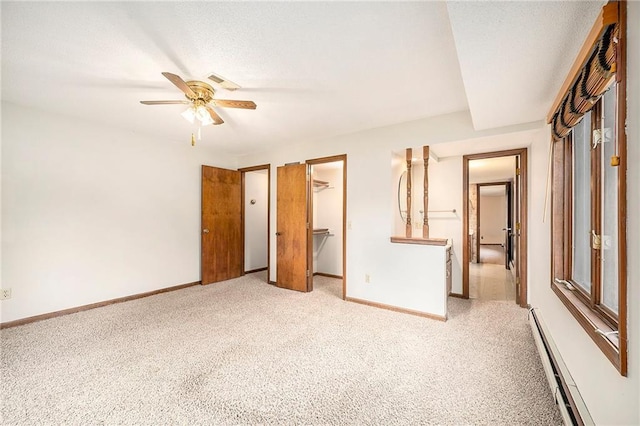 unfurnished bedroom with a spacious closet, light colored carpet, a closet, ceiling fan, and a baseboard heating unit