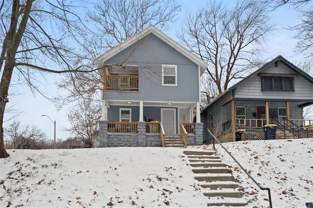 snow covered back of property with a balcony and a porch