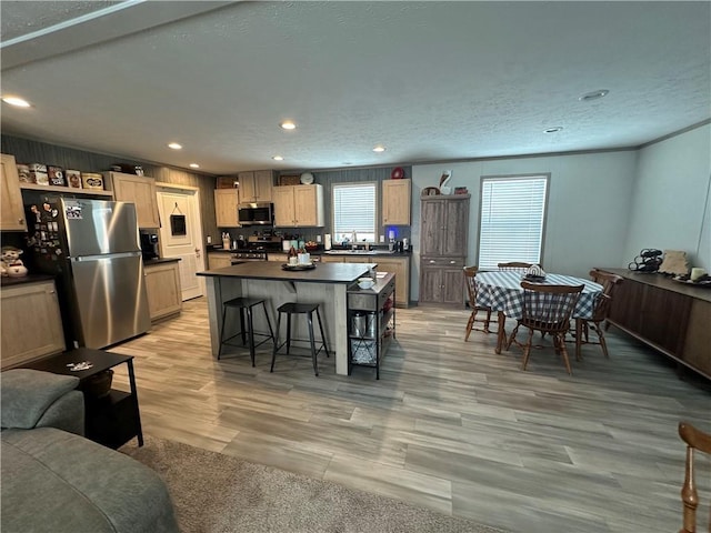 kitchen with a kitchen breakfast bar, a kitchen island, dark countertops, stainless steel appliances, and light wood-style floors