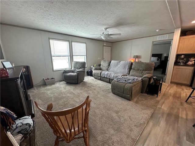 living area with visible vents, crown molding, light wood-style flooring, a textured ceiling, and a ceiling fan