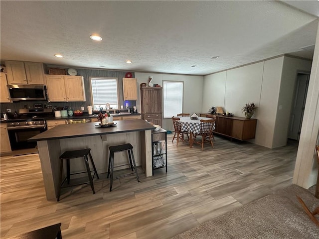 kitchen featuring a breakfast bar area, light wood finished floors, stainless steel appliances, dark countertops, and a center island