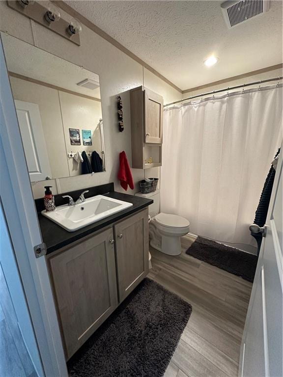 bathroom featuring visible vents, toilet, vanity, wood finished floors, and a textured ceiling