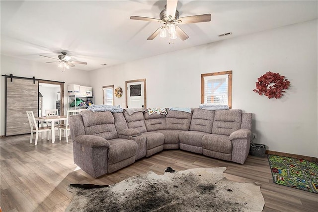 living room with a barn door, light wood-type flooring, and ceiling fan