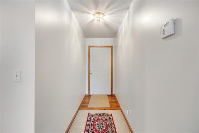 hall featuring a textured ceiling, light carpet, and baseboards