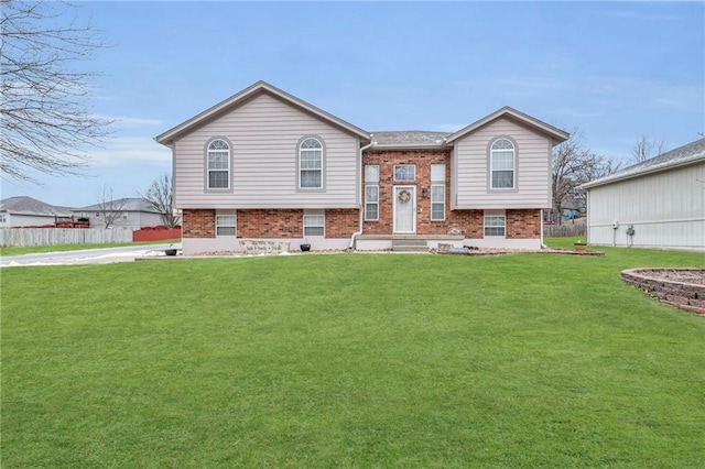 split foyer home with a front yard, fence, and brick siding