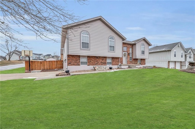 raised ranch featuring a front yard, brick siding, and fence